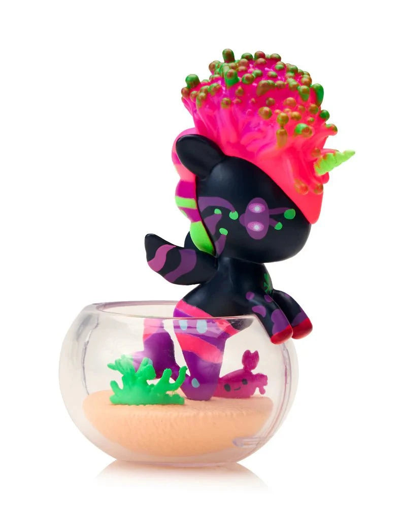 The tokidoki (IT) Neon Reef Mermicorno Blind Box features a vibrant unicorn figure with neon pink, green, and purple highlights in a clear bowl with sand and green accents—ideal for any collectible display.