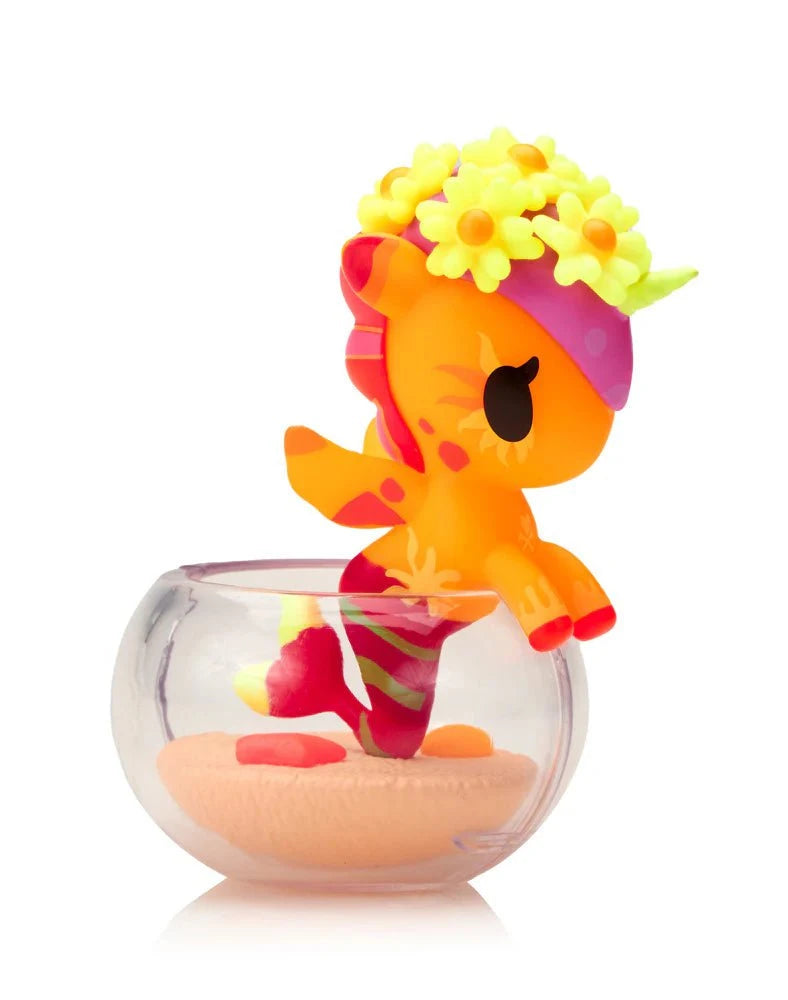 The Tokidoki Neon Reef Mermicorno Blind Box by tokidoki (IT) features a small orange and pink unicorn figurine with a flower crown in a clear sand-filled container, designed to glow under blacklight.