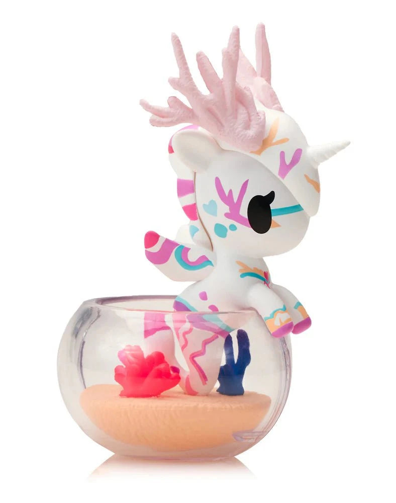 The Tokidoki Neon Reef Mermicorno Blind Box by tokidoki (IT) features a vibrant unicorn figurine with coral-like horns, standing in a clear bowl filled with sand and coral decorations.