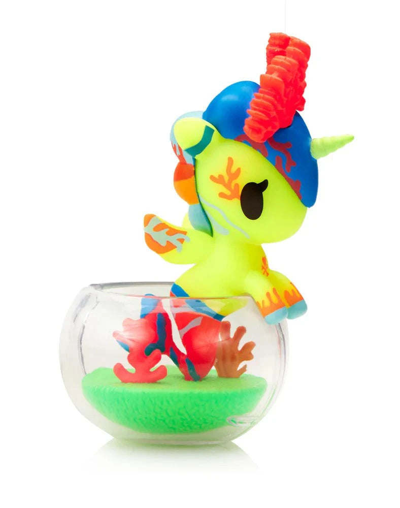 The Tokidoki Neon Reef Mermicorno Blind Box by tokidoki (IT) features a small, brightly colored unicorn figurine with coral details in a clear round bowl with green and red accents that glows under blacklight.