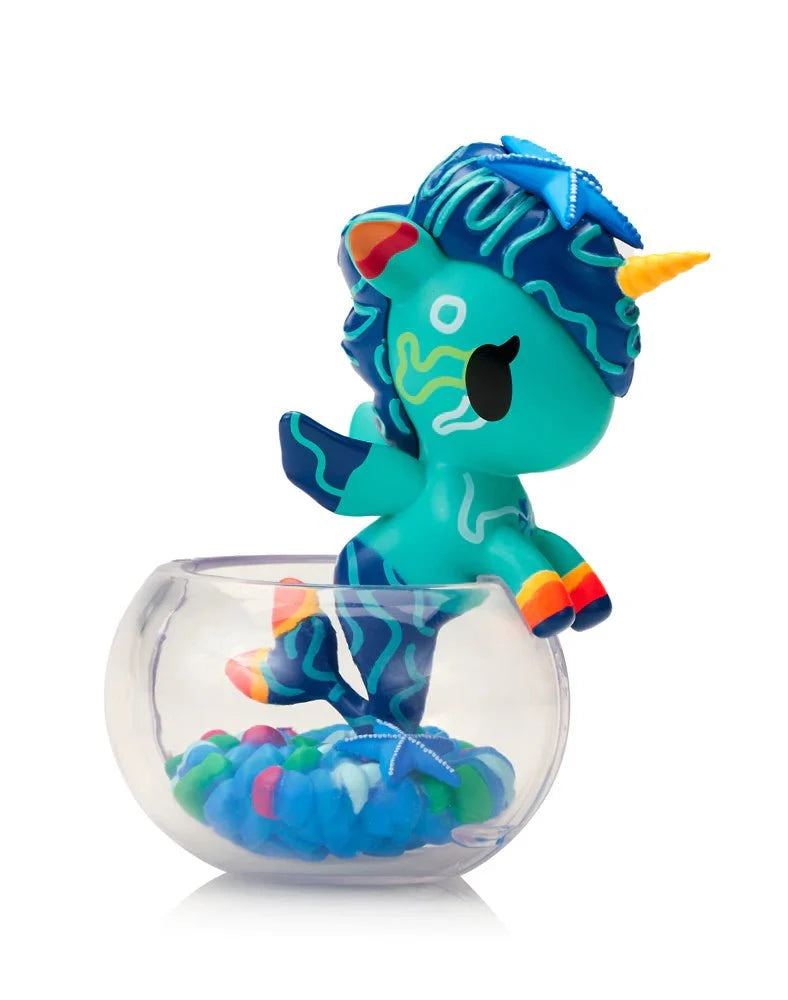 The tokidoki (IT) Neon Reef Mermicorno Blind Box features an aquatic-themed figurine that sits in a clear bowl with colorful pebbles and glows under blacklight.