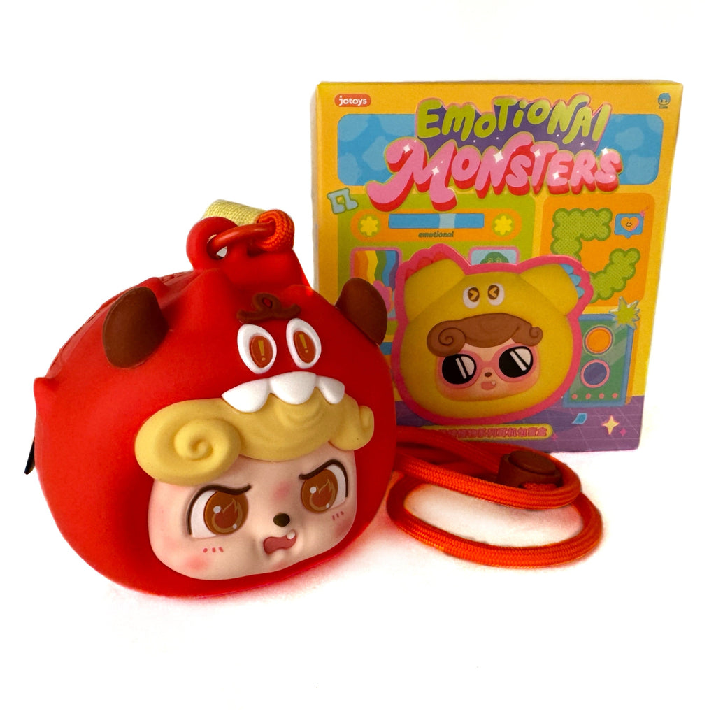 A round red Q.Kid Emotional Monster Headphone Bag by Jotoys, featuring a cartoon monster face with horns and yellow hair, sits before a colorful