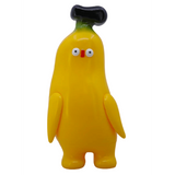 Banana Boo - Yellow by Rotofugi is a cute, banana-shaped plush collectible with small arms, wide eyes, a red nose, and a black-tipped head—standing upright against a plain background.