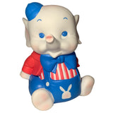 The Carnival Stripes Baby Elephant by Bitter Squeaks (US) is a cartoon-style stuffed animal wearing a blue hat, red jacket, blue bowtie, and blue overalls with a white bunny on the front, sitting upright.