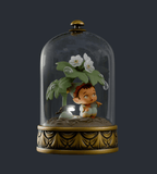 The Cloche Fairies Blind Box by Kaleidos Creative features a small LED lantern figure of a child with leaves and white flowers, illuminated softly under a glass dome with a gold base.