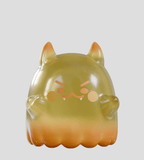 An orange-yellow cat-like figurine with small fangs, round cheeks, and an angry expression from the Cute as Heck! Blind Box by Kaleidos Creative, shown against a plain light gray background.