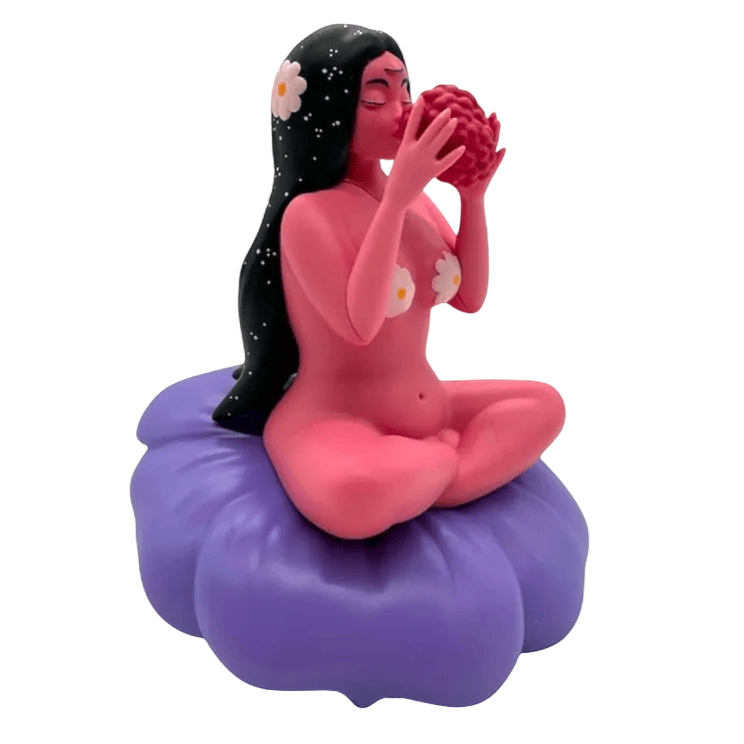 Flower Girl by UVD Toys (US) features a pink-skinned figure with long black hair and white flowers, sitting cross-legged on a purple cushion while holding red fruit—an eye-catching collectible or unique gift.
