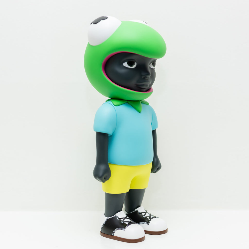 This limited edition 3D vinyl figurine, Phibby — OG (Green), features dark skin, a frog-shaped helmet, a blue shirt, yellow shorts, and black shoes with white laces. Influenced by Hebru Brantley's unique style, this figure from Hebru Brand (US) stands against a plain white background.