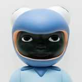 A close-up of Phibby — Purple, a limited edition figurine by Hebru Brand (US), featuring a dark face, large eyes, and a blue helmet resembling a frog's head with prominent eyes on top. The figurine’s body is also blue with a simplistic design, reminiscent of iconic characters created by Hebru Brantley.