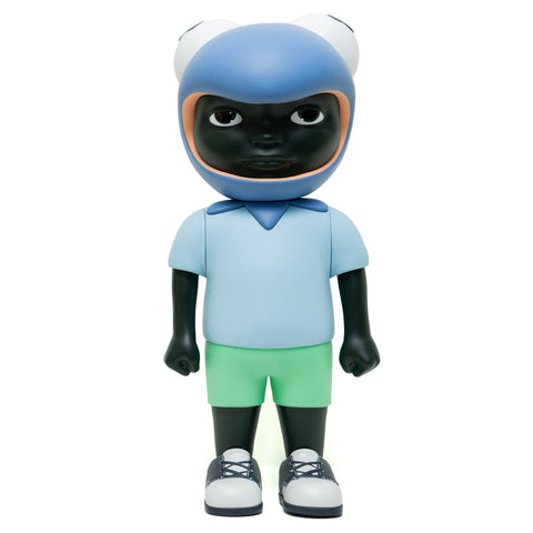 A stylized figure from Hebru Brand's limited edition release, "Phibby — Purple," is depicted wearing a blue frog helmet, light blue shirt, green shorts, and white sneakers. The figure has a dark complexion and a neutral expression that echoes Hebru Brantley's iconic characters.