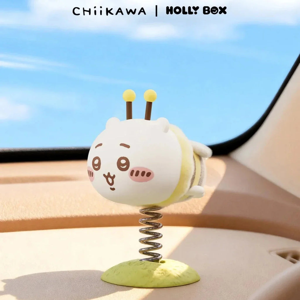 A Chiikawa Little Bee Wobble Figure dressed as a bee mounted on a coiled metal spring on a car dashboard.