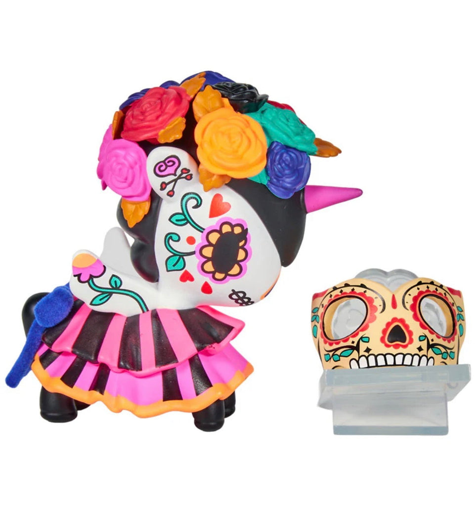 The Tokidoki Unicorno After Dark Masquerade Blind Box features a collectible toy with a colorful flower crown, heart and swirl face designs, pink horn, and skirt, displayed next to a decorative skull mask—ideal for any Blind Box fan.