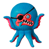 The VAG 40 β AHOY by Shelterbank, a vibrant Japanese vinyl toy from Medicom (JP), showcases an octopus-like creature adorned with an eyepatch, sharp teeth, and a protruding tongue. This colorful figure features blue, red, and pink hues and is a charming addition to the world of Vinyl Artist Gacha collectibles.