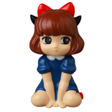The VAG 40 β Zombiecats Story Morimeiworks Nekomusume from Medicom (JP) features a charming cartoon character with brown hair, a red bow, and a blue dress adorned with a white collar. This delightful vinyl toy sits gracefully on the ground with hands placed gently in front, encapsulating the playful essence of Japanese gachapon figures.