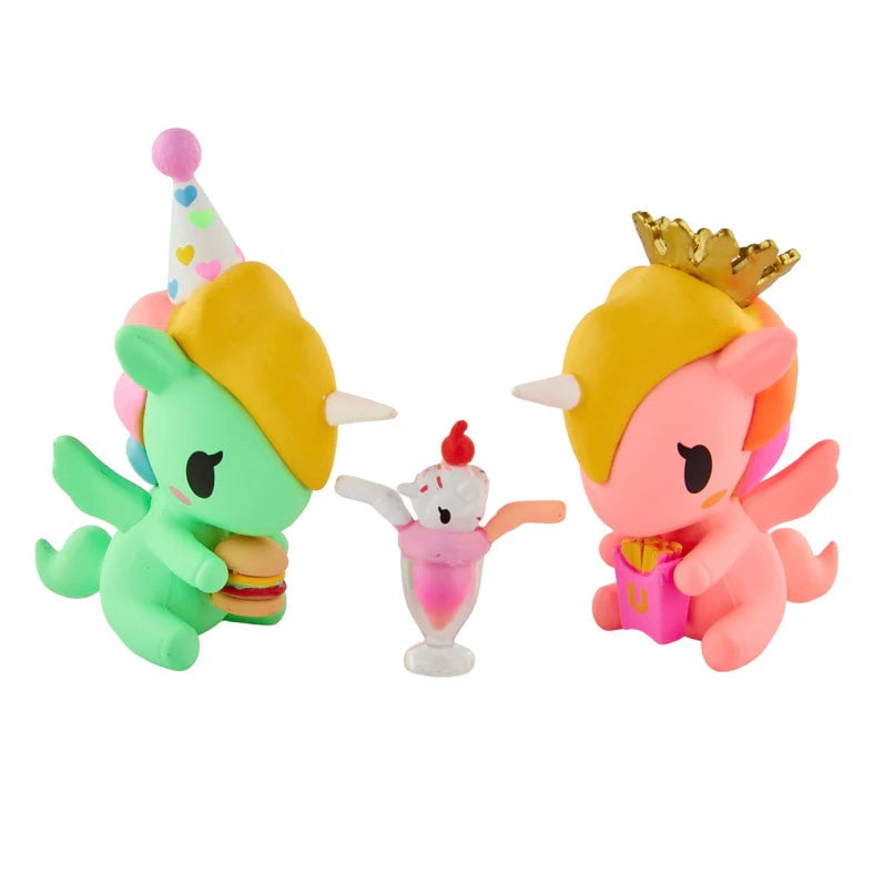 Two playful tokidoki Twinsies Unicorno Blind Box figures—one green with a party hat and burger, one pink with a crown and gift—sit beside a mini ice cream sundae for a delightful surprise collectible set.
