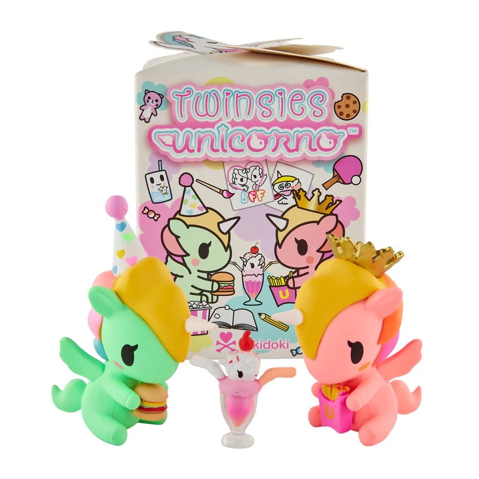 Two vibrant tokidoki Unicornos with hats sit next to a dessert and a pastel Tokidoki Twinsies Unicorno Blind Box, decorated with playful illustrations from tokidoki.