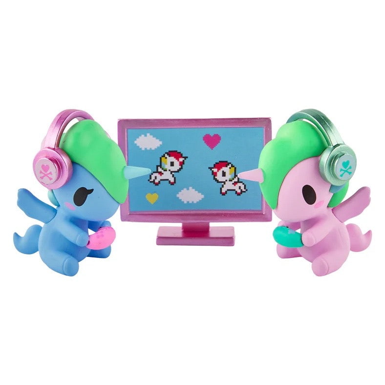Two vibrant Tokidoki Twinsies Unicorno Blind Box figures by tokidoki wear headsets and play video games together, their eyes on a screen of pixelated unicorns and hearts—an irresistible addition to any blind box surprise!.