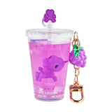 A clear cup from the tokidoki Beverage Besties Unicorno Blind Box holds purple liquid, a small purple unicorn toy, and a grape-shaped keychain—perfect for tokidoki fans!.