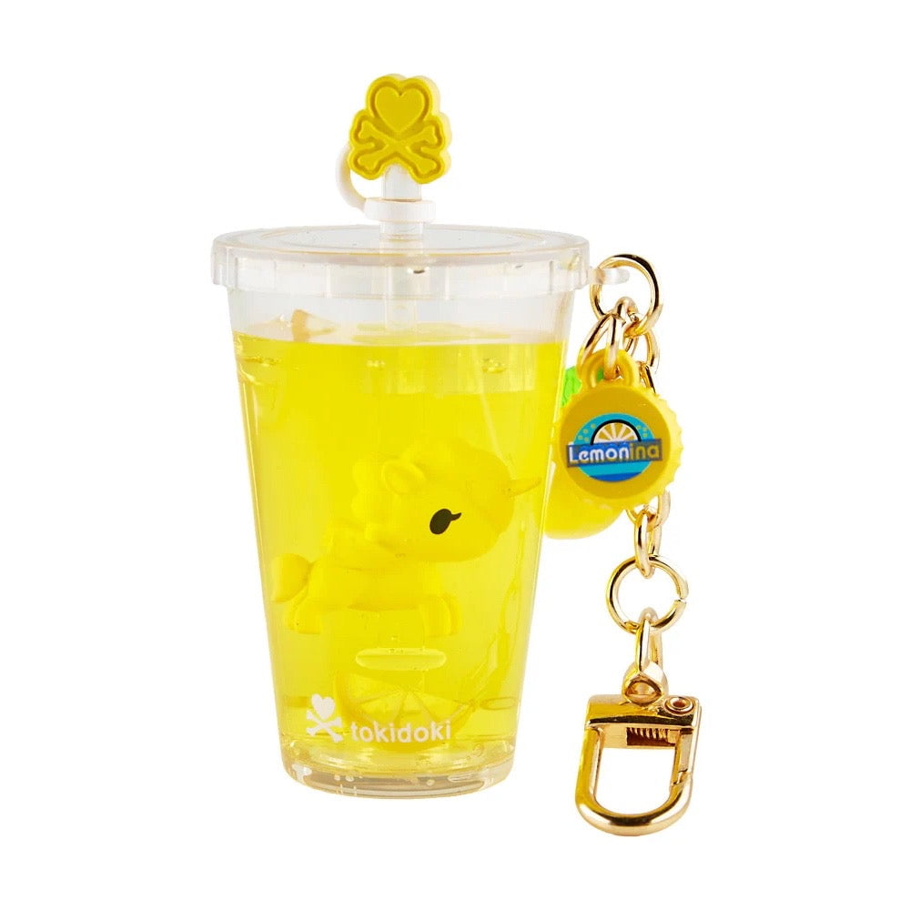 A clear cup with yellow liquid and a small yellow character inside, labeled Lemonina, featuring a yellow clover on the lid and gold keychain clip—part of the Tokidoki Beverage Besties Unicorno Blind Box by tokidoki.