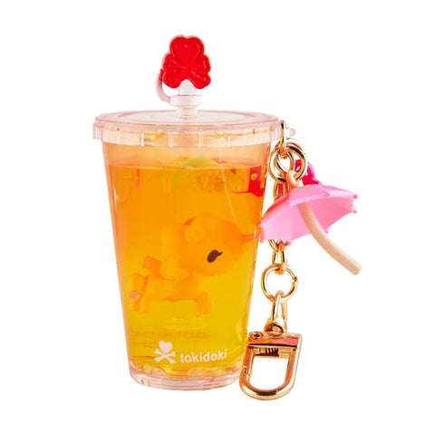 The Tokidoki Beverage Besties Unicorno - Tropical Fizz (Special Edition) keychain features a clear cup with a yellow lion, red heart straw, and pink umbrella charm on a gold clasp, capturing the vibrant look of a sparkling citrus drink.
