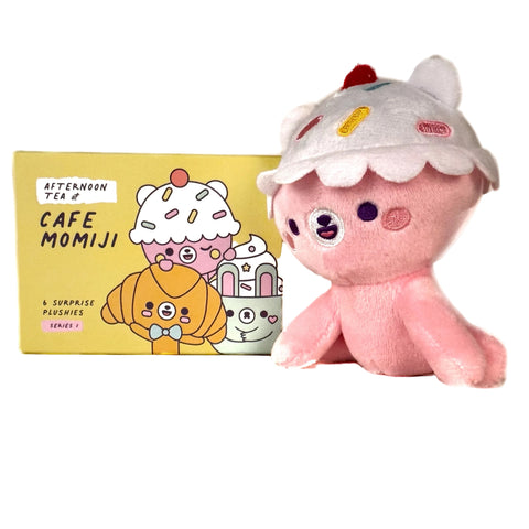 A cute plush with a cupcake hat sits next to a yellow Momiji Cafe Momiji Blind Box, featuring cartoon dessert characters from the "Afternoon Tea at Cafe Momiji" collection.