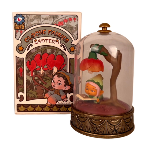 A collectible fairy figurine reads under a flower-shaped LED lantern inside a glass dome. The illustrated box, labeled "Cloche Fairies Blind Box" by Kaleidos Creative, makes this a charming find for cloche fairy or blind box collectors.