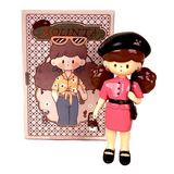 A stylish girl doll with brown hair, a black beret, and a pink outfit stands before a Finding Unicorn Molinta Retro Girls Blind box, which features an illustrated character wearing sunglasses and a yellow shirt.