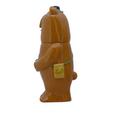 Side view of Paradise Toy's Kurichan- Milktea, a brown bear-shaped plastic toy with a small yellow bag and black button on its head, perfect for collectible plush toy fans, shown against a white background.