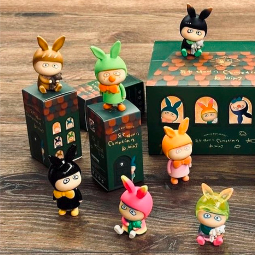 A How 2 Work blind box series featuring a group of small figurines, including A Boy - Sit Down Comedian and B. Wing, all neatly packed in a box.