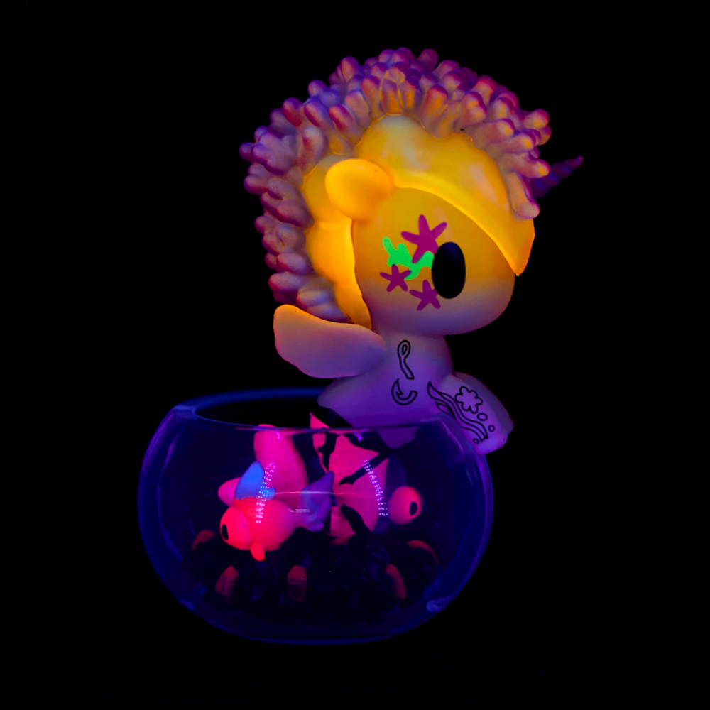A tokidoki (IT) Neon Reef Mermicorno toy from the Tokidoki Neon Reef Mermicorno Blind Box glows beside luminous toy fish, all shining brightly under blacklight.