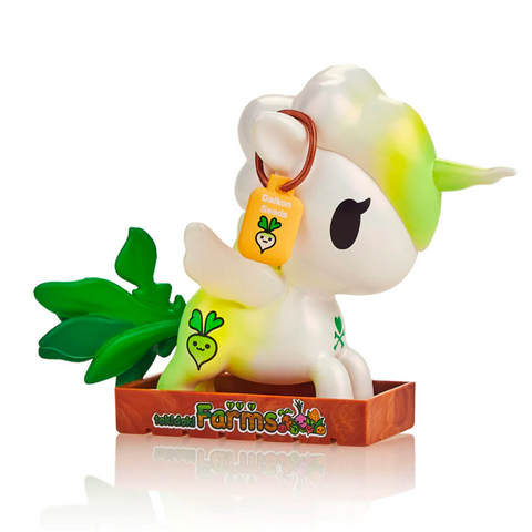 A colorful unicorn figurine with a green mane, standing in a brown planter, holding a carrot labeled "Tokidoki Veggie Unicorno - Daikon.
