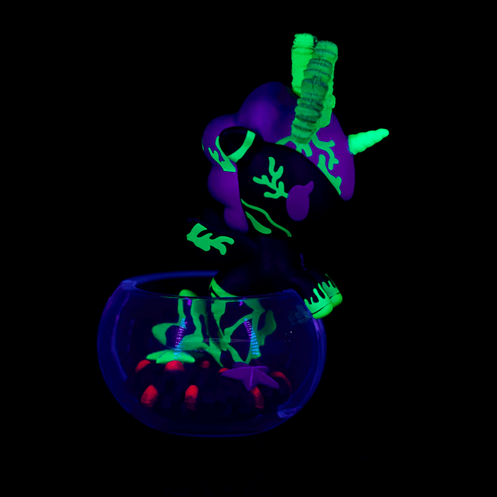 The Tokidoki Neon Reef Mermicorno - Deep Star Coral Special Edition features a glow-in-the-dark unicorn with neon green and purple designs in a transparent bowl, glowing under blacklight.