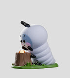 A fuzzy collectible from the Kaleidos Creative Wooly Bear and Friends Vinyl Blind Box features a cartoon-style Wooly Bear caterpillar with black antennae and pink cheeks, leaning on a tree stump with an orange object, set on a green base.