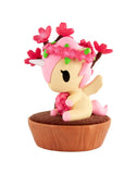 A charming unicorn figurine with pink hair, a flower crown, and wings sits on a brown base—ideal for miniature gardens or as part of the tokidoki Botanical Bonsai Unicorno Blind Box by tokidoki.
