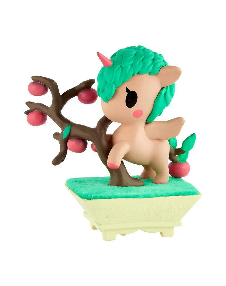 The Tokidoki Botanical Bonsai Unicorno Blind Box by tokidoki features a small, pastel figurine with green hair beside an apple tree on a grassy base—ideal for Blind Box Collection fans and miniature garden toy enthusiasts.