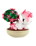 The tokidoki Botanical Bonsai Unicorno Blind Box includes a small white Unicorno with pink accents and flowers, posed by a green bonsai tree in a beige pot—ideal for miniature garden toy displays.