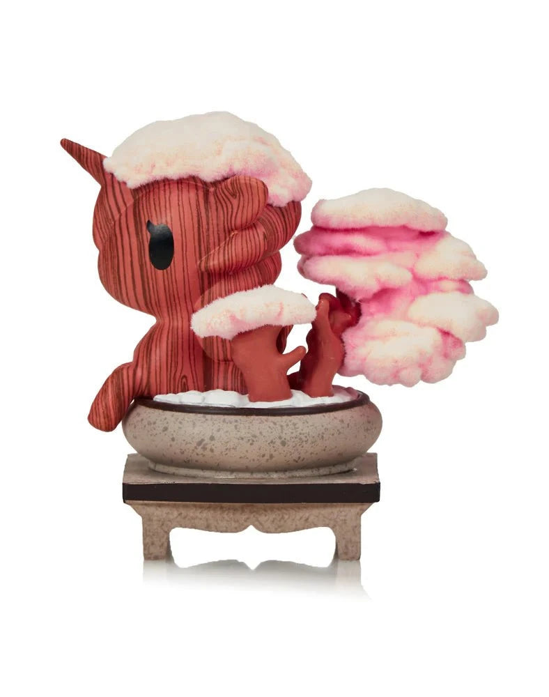 The Tokidoki Botanical Harmony Unicorno - Cherry Blossom Serenity (Special Edition) features a horned Unicorno in a pot next to pink, snow-covered cherry blossom trees, all on a small pedestal for botanical harmony.