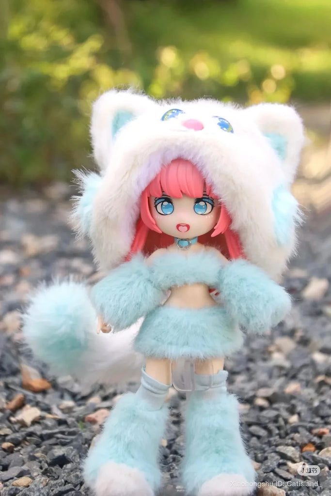 A BIJIDI Cat Island — Black Cat Or Candy Cat? Blind Box ball-jointed doll with pink hair wears a fluffy blue and white cat-themed outfit with hood and ears, standing on gravel with greenery in the background.