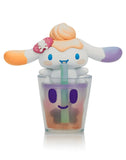 A Tokidoki x Cinnamoroll Sweet Treats Blind Box figure with long ears, orange and purple accents, and a swirl on its head sits atop a smiling cup with green straw—a charming collectible from Tokidoki.