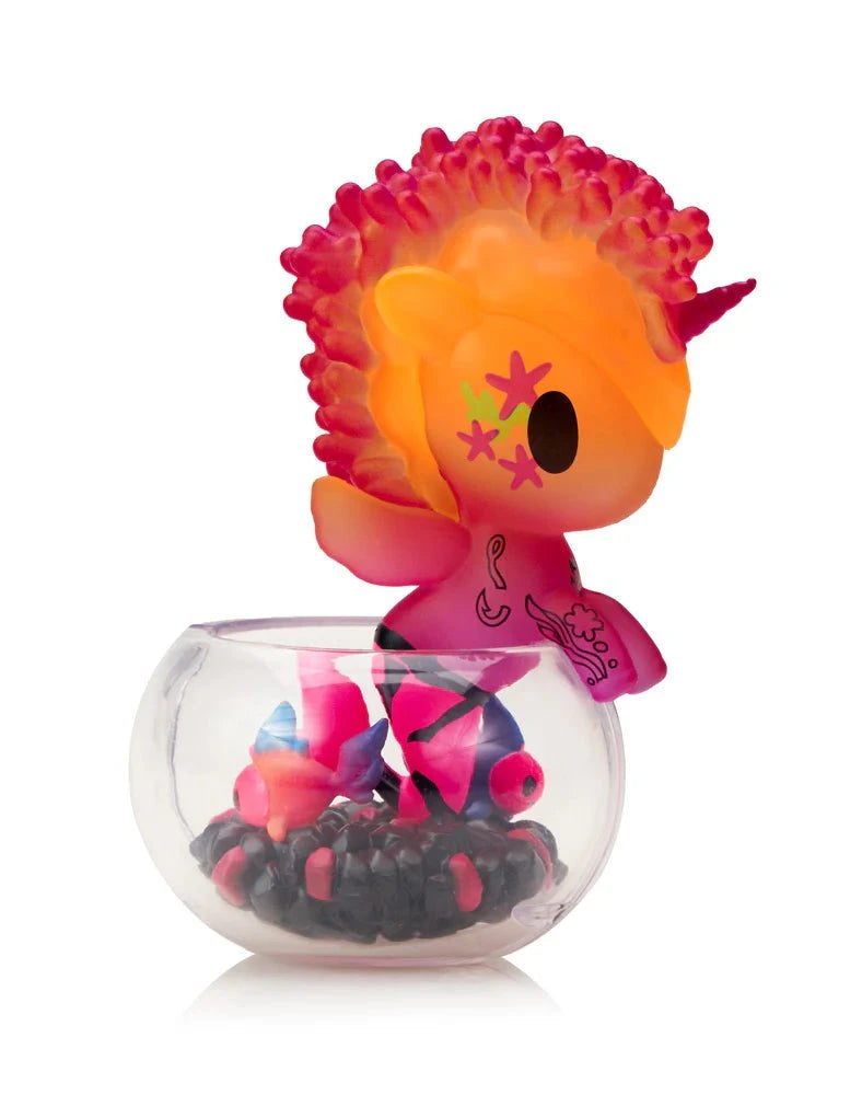 The tokidoki (IT) Neon Reef Mermicorno Blind Box features a small, vibrant figurine with a pink and orange mane in a clear container with toy fish and black pebbles—it glows under blacklight for an extra dazzling surprise.