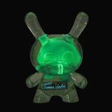 The Kidrobot Infected Specimen Dunny 8” GID Art Figure (LE 600) glows green with bubble details against a black background, featuring handwritten text on its torso to highlight its limited edition status.