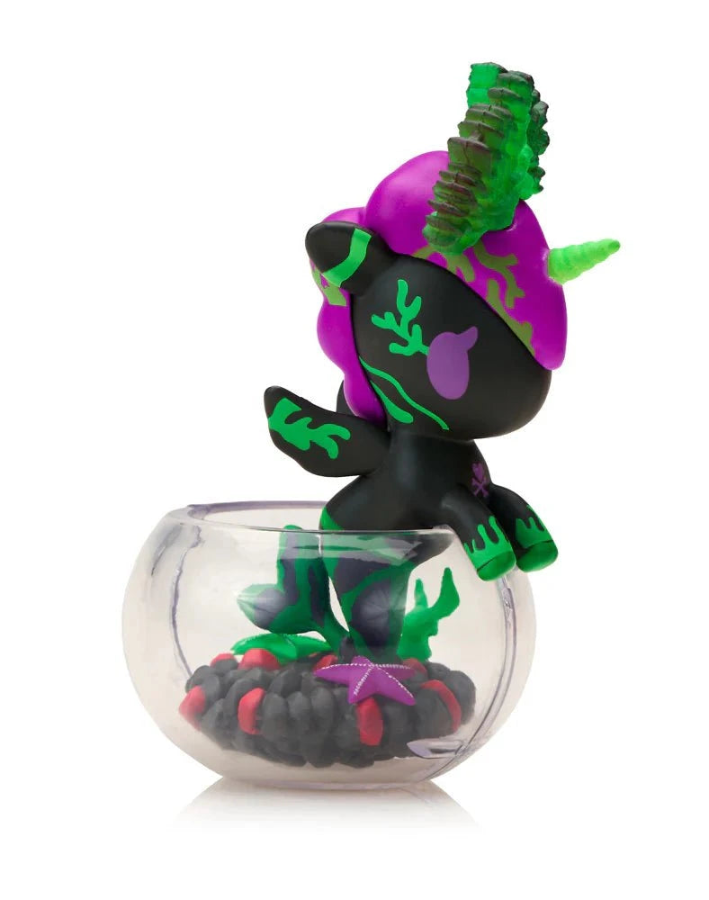 A small Tokidoki Neon Reef Mermicorno - Deep Star Coral Special Edition figurine stands in a clear bowl filled with black and red objects and green plant shapes.