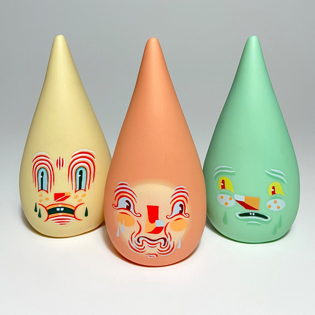 Three cone-shaped figurines called Mini Driplets — Primo & Plebe Blind Box by Squibbles Ink + Rotofugi (US) with expressive painted faces in yellow, orange, and green colors stand side by side against a plain background.