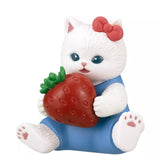 From Kitan Club's Mofusand x Sanrio Series 2 Capsule (Set of 5), this Sanrio character cat with a red bow and blue outfit sits holding a strawberry, showing pink paw pads.
