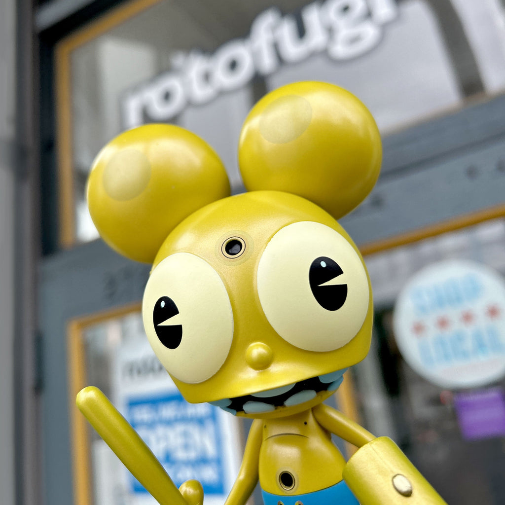 A vinyl version of Dalek Space Monkey — Gold Rotofugi Exclusive holding a sword in front of a store by UVD Toys (US).