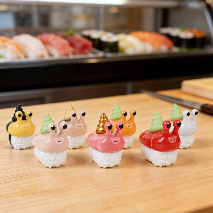 Rotofugi’s Sushi Snails Blind Box figures—adorable snail-like creatures on sushi—are displayed on a wooden counter with sushi dishes.
