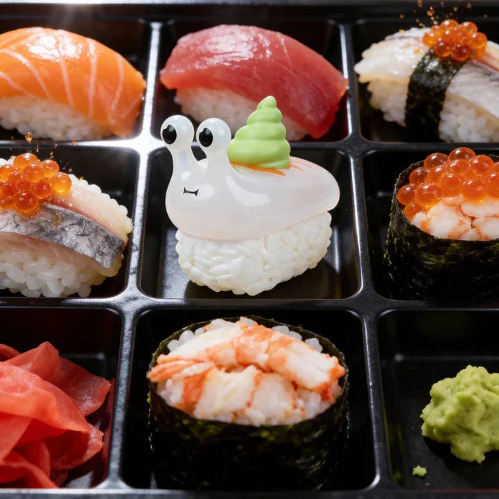 The Rotofugi Sushi Snails Blind Box features assorted sushi pieces, including a playful snail-shaped creation made of rice, fish, and wasabi, alongside traditional sushi selections.