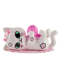 A white cartoon cat figurine from the Tokidoki Cherry Blossom Cats- Single Blind Box by Tokidoki, with green eyes and pink flower accents, lies on its back holding a pink yarn ball—perfect for celebrating cherry blossom season.