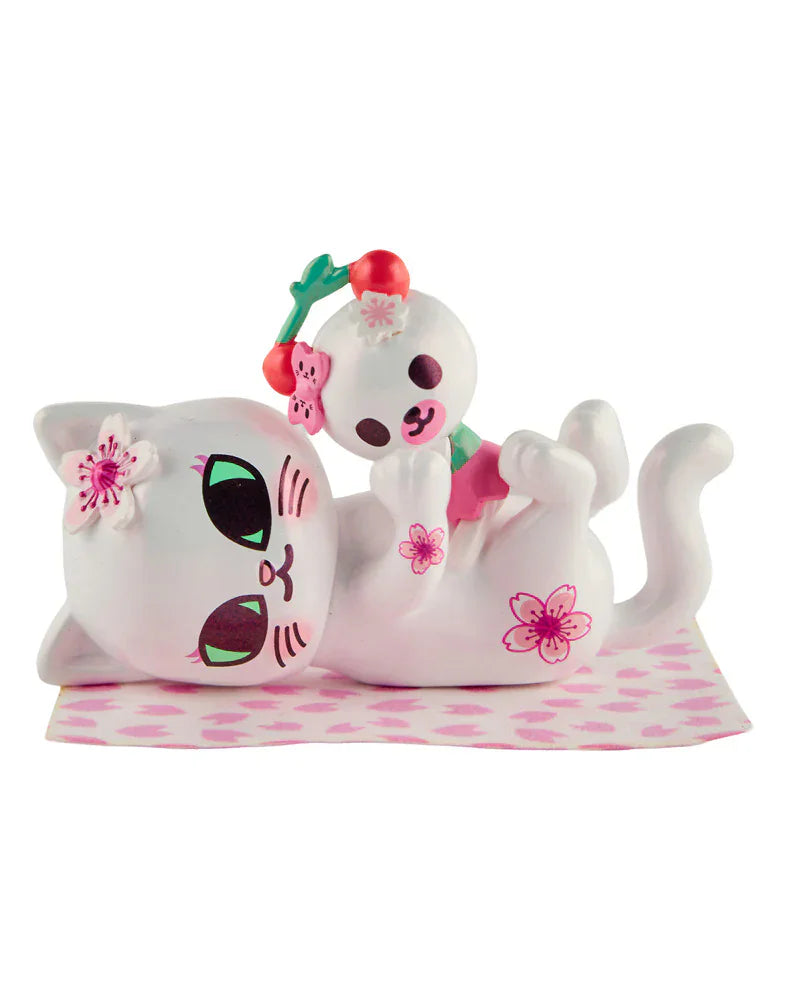 A Tokidoki Cherry Blossom Cats- Single Blind Box figurine features a white cat with green eyes, pink markings, and a flower, plus a bear with a cherry headband. Perfect for fans of Tokidoki and cherry blossom season!.