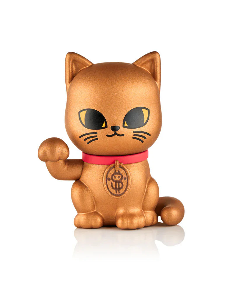 The Tokidoki Lucky Cats Blind Box by tokidoki (IT) features a golden collectible kitty figurine with a raised paw, black eyes, red collar, and coin symbol on its chest, inspired by traditional lucky cats. Set against a white background.
